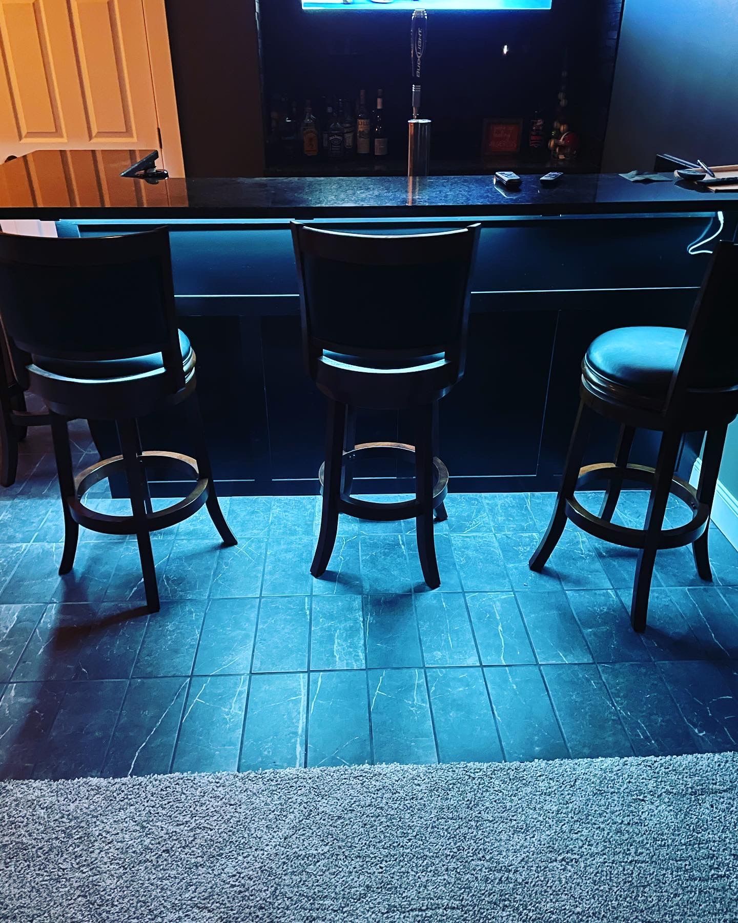 Three black bar stools at a dark bar with illuminated blue accents.
