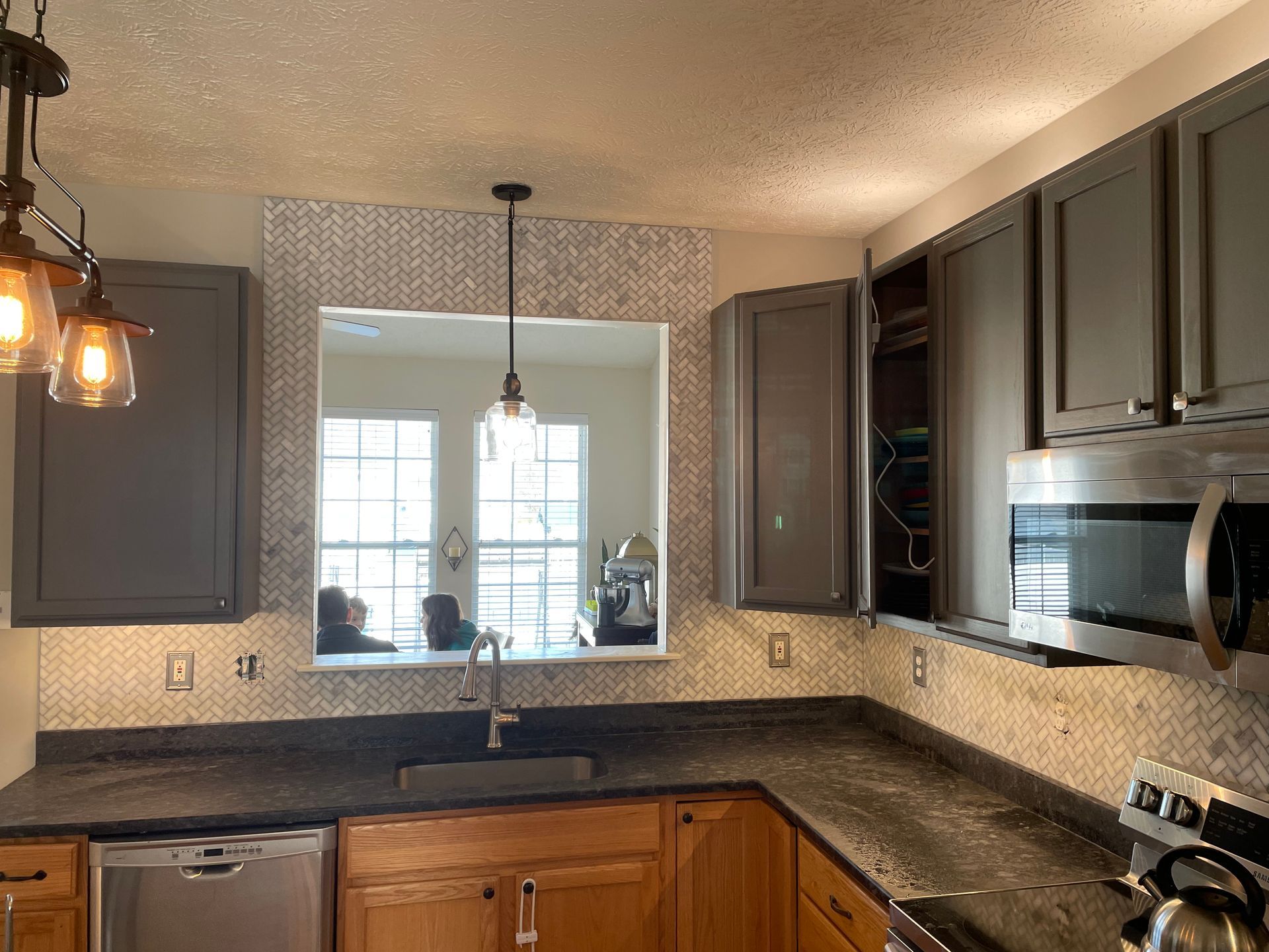 Kitchen with gray cabinets, dark countertops, and a window with mosaic tile backsplash.