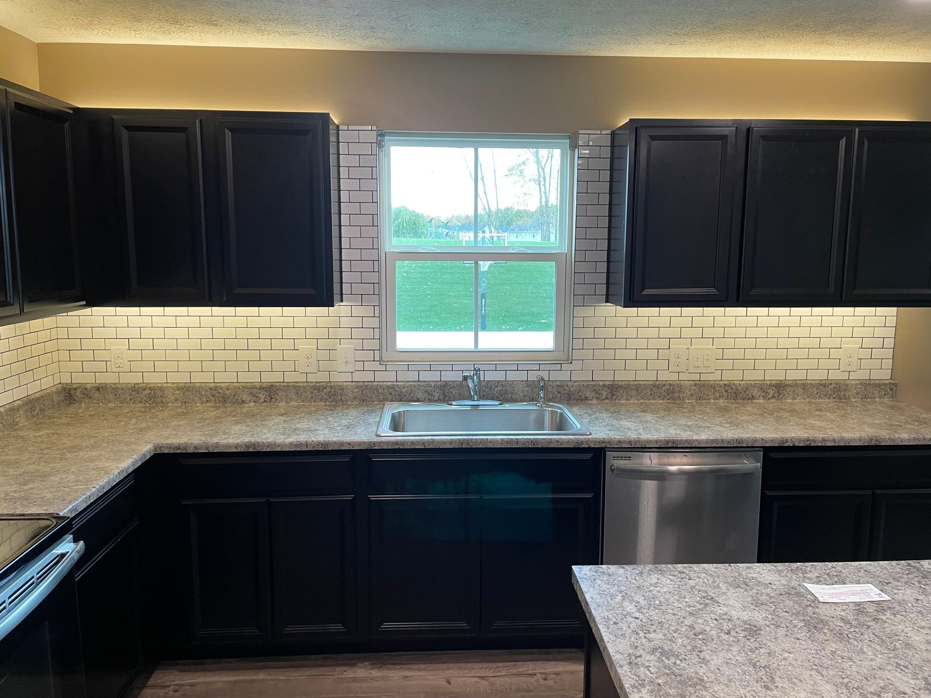 Kitchen with black cabinets, white and gray backsplash, and stainless steel appliances.