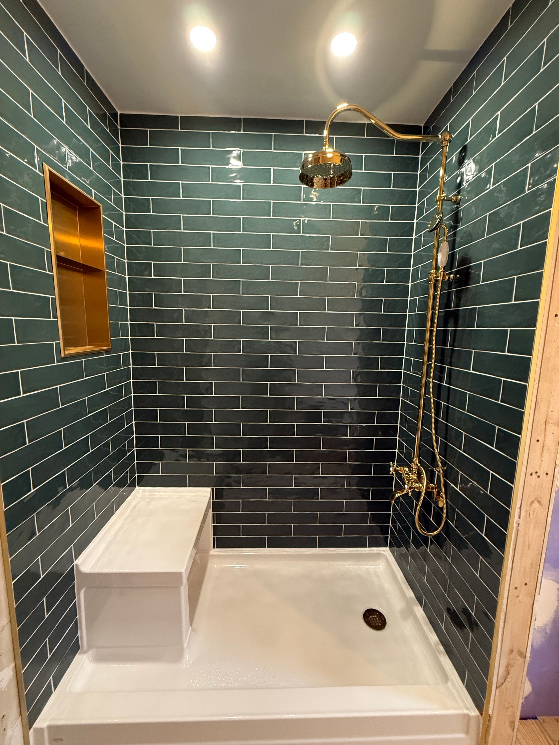 Green tiled shower with gold fixtures, a built-in seat, and a recessed golden shelf.