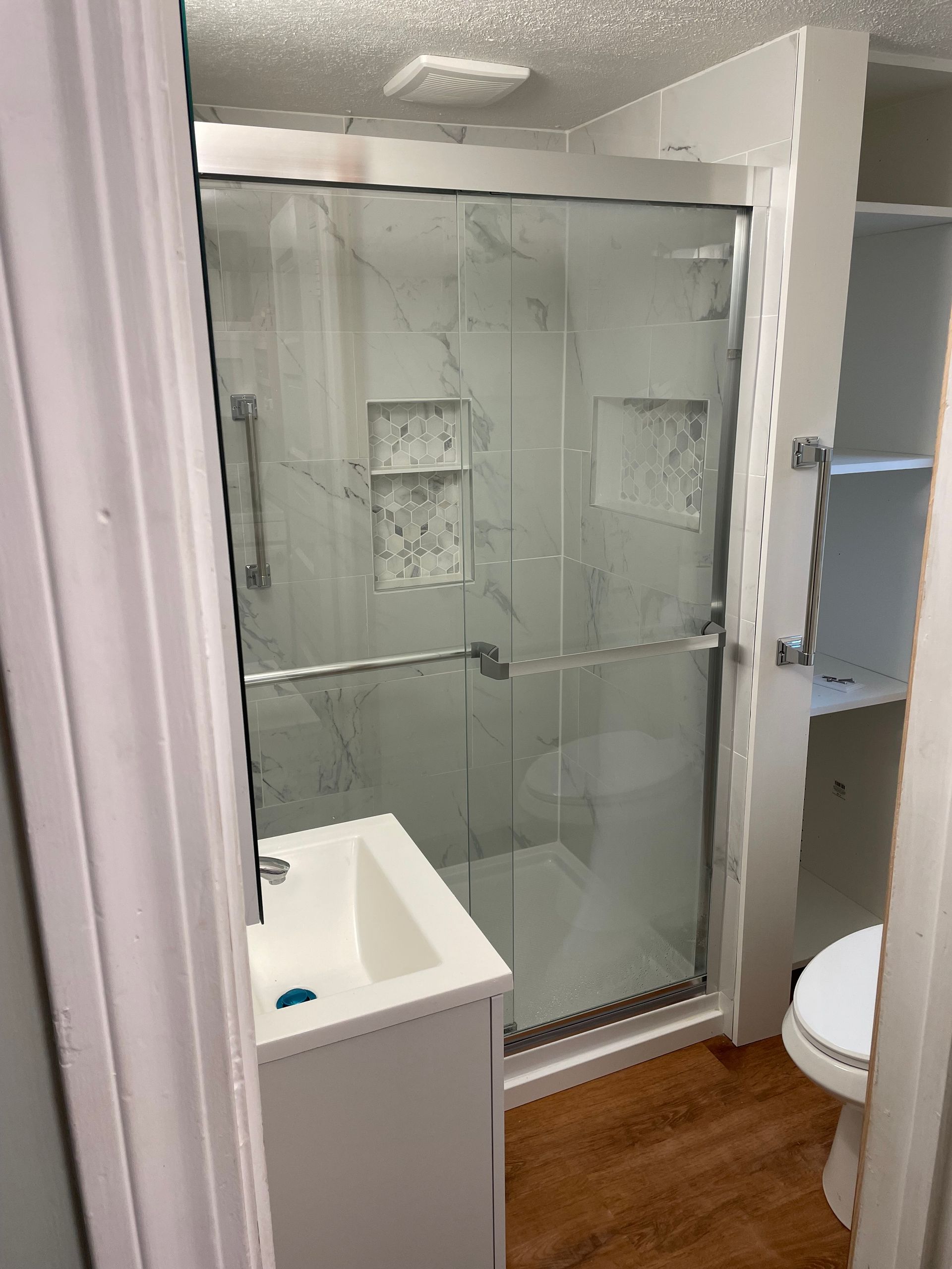 Bathroom with a white vanity, a marble-tiled shower, and a toilet; a doorway to the room.