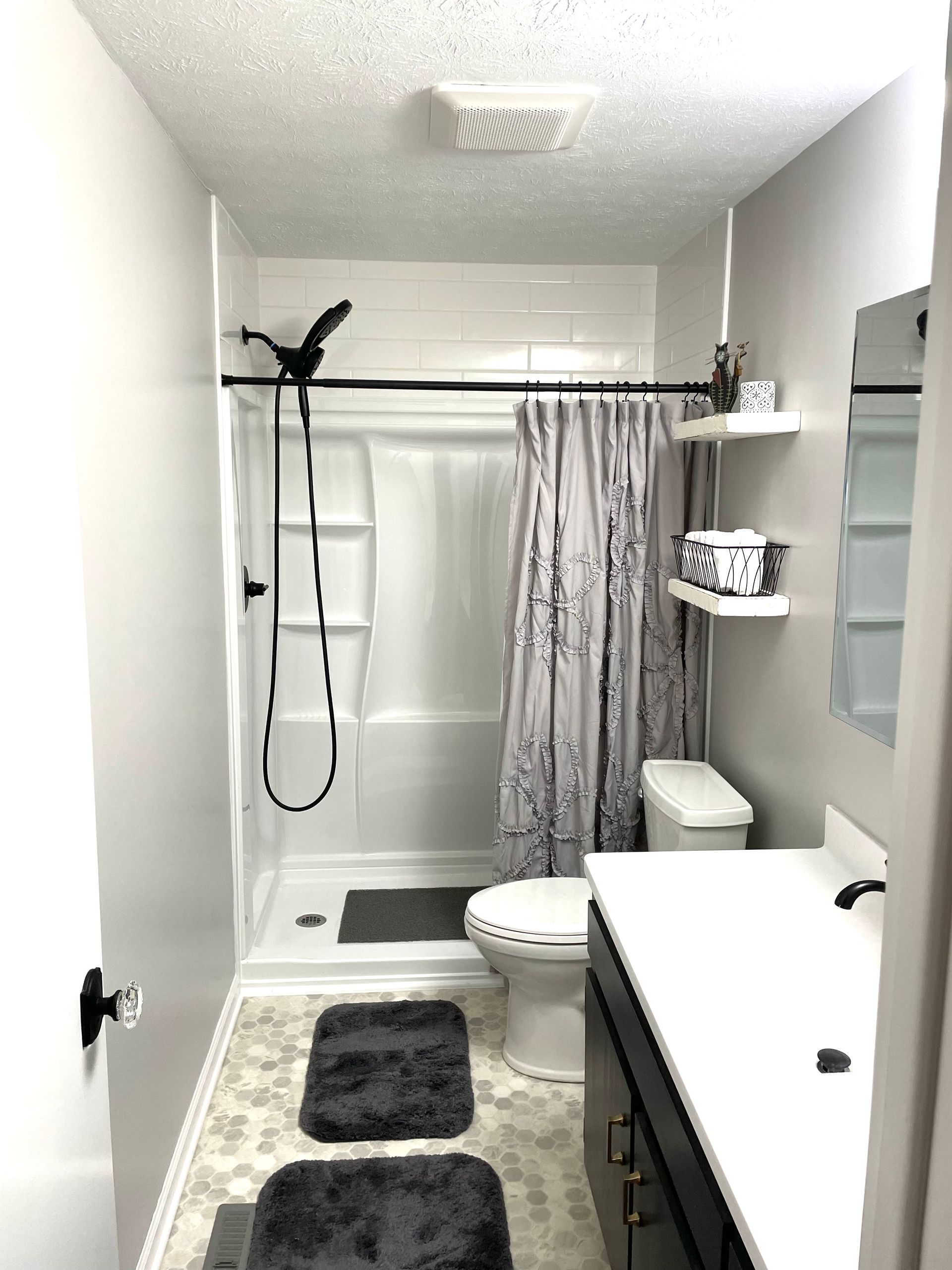 Bathroom with white tile shower, gray walls, black fixtures, and patterned shower curtain.