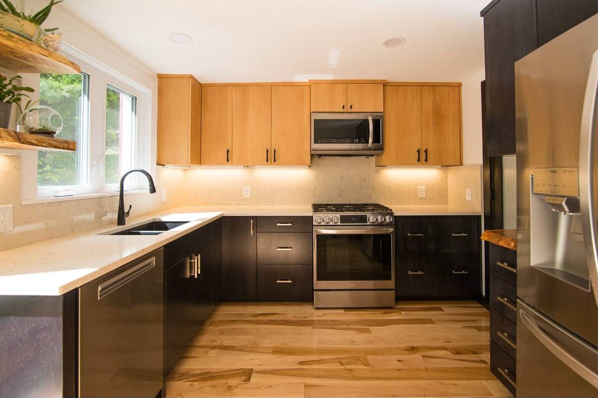 Modern kitchen with light wood upper cabinets, dark lower cabinets, stainless steel appliances, and wood floors.