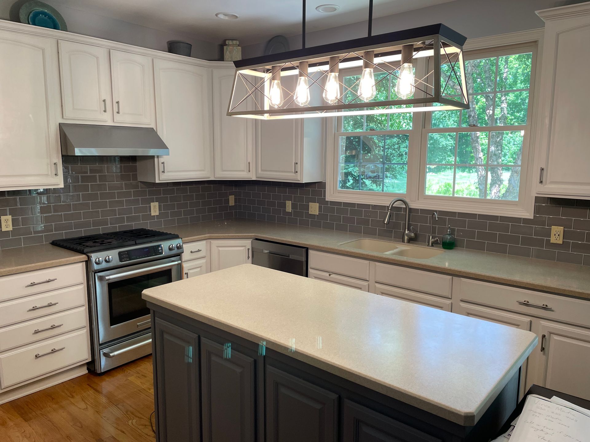 Kitchen with white cabinets, gray backsplash, stainless steel appliances, and a gray island with a light countertop.