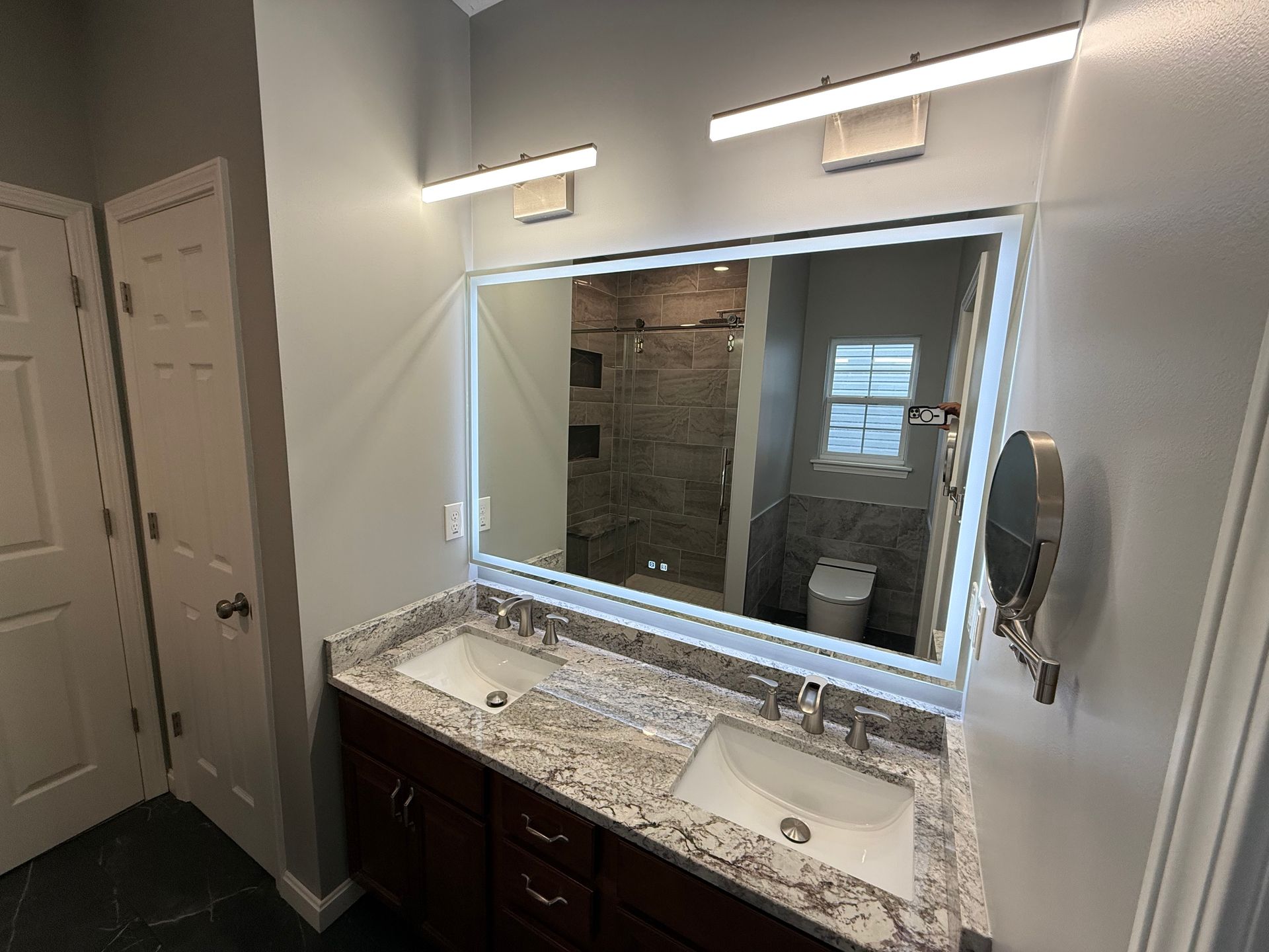 Bathroom with double sinks, large mirror, and overhead lighting. Dark brown cabinets and granite countertop.