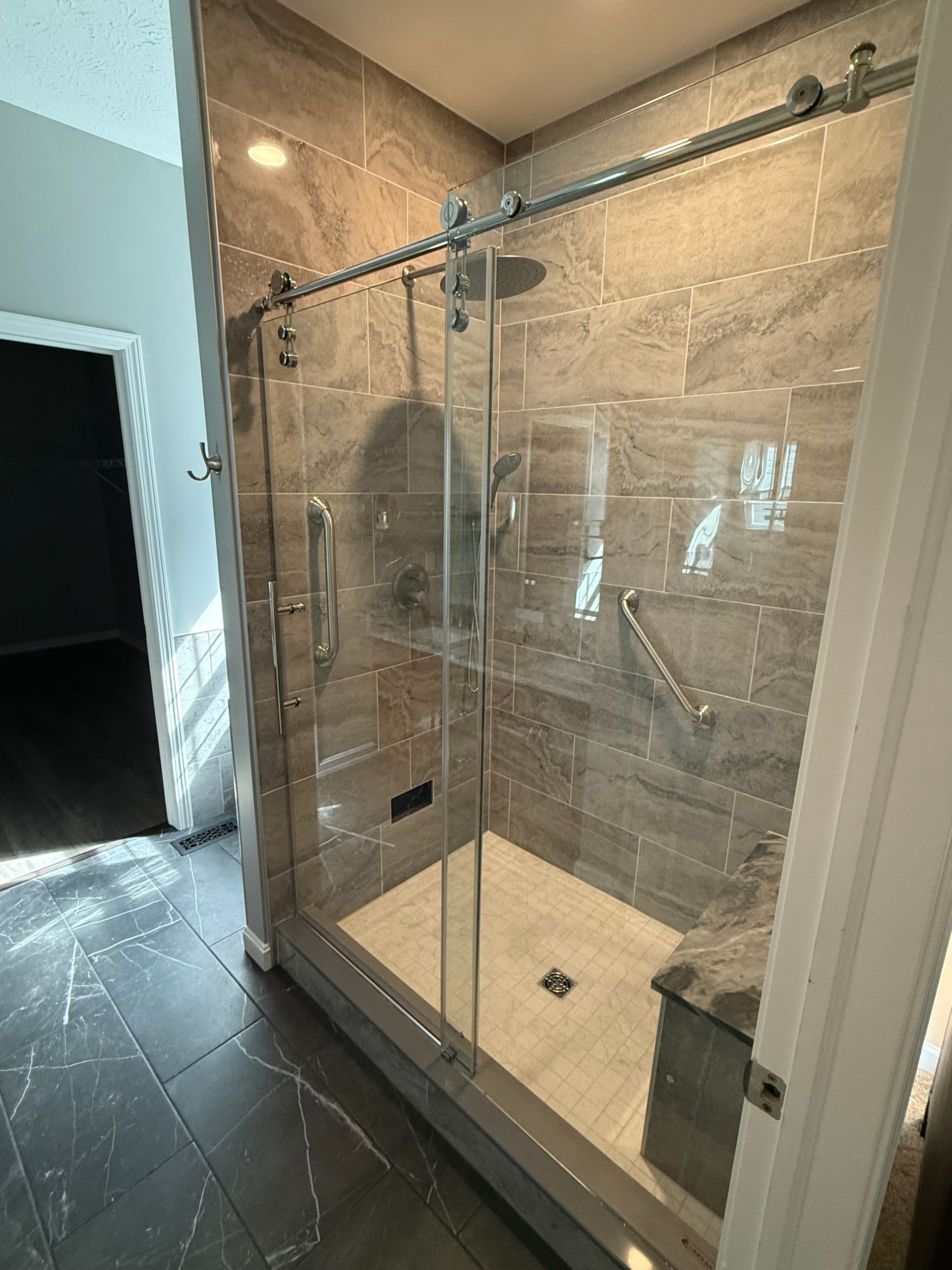 Modern shower with sliding glass doors, gray tiled walls, and a built-in bench.