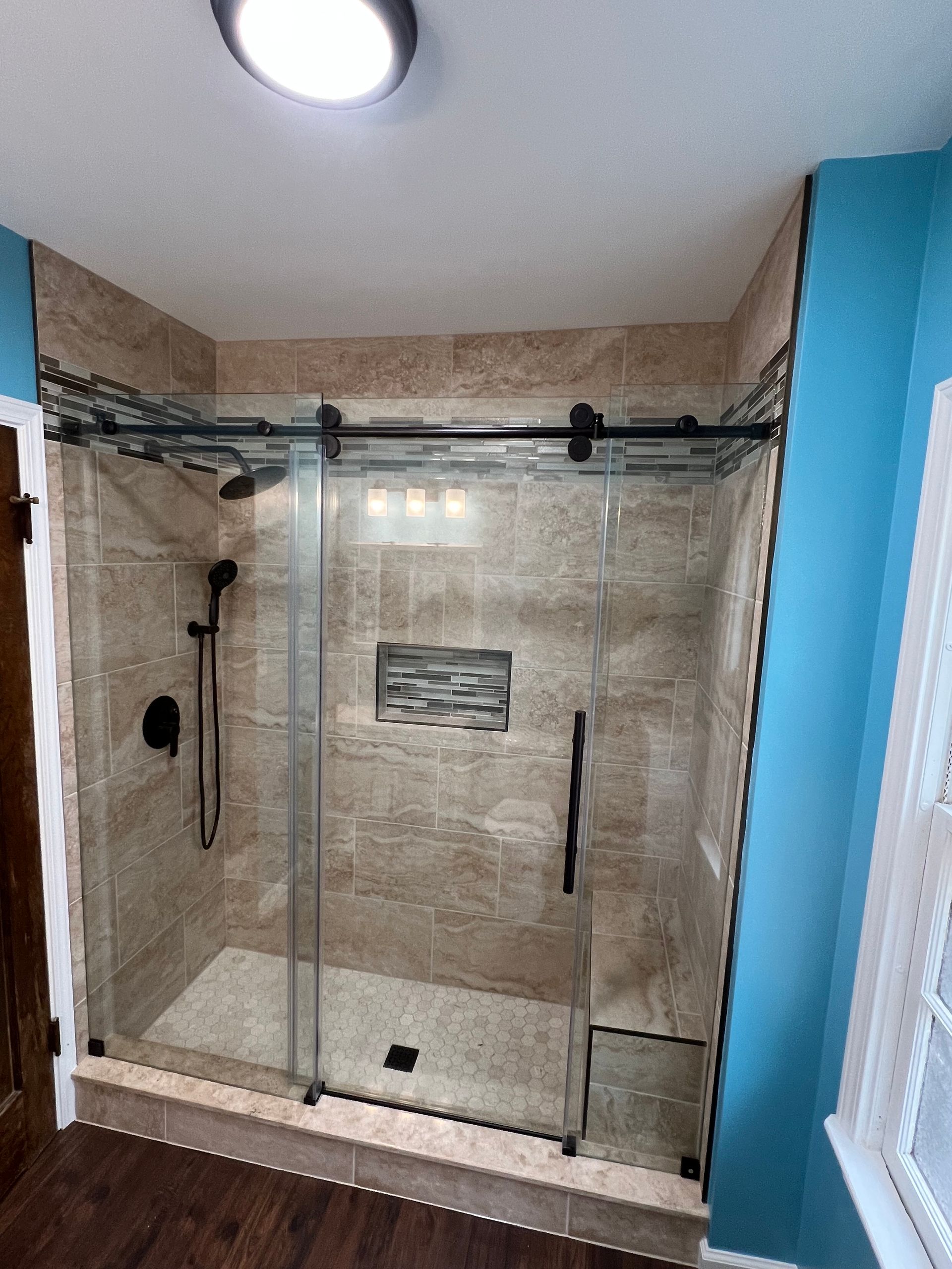 Shower with sliding glass doors, tan tile, black fixtures, and blue walls.