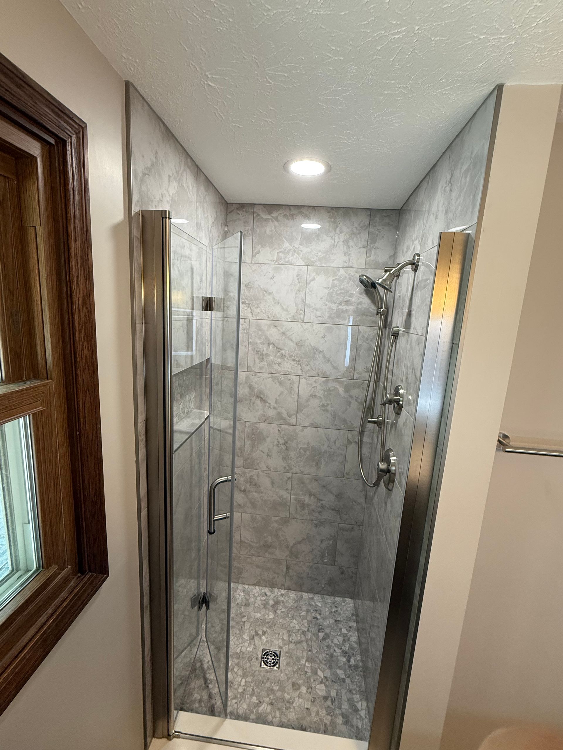 Shower stall with marble-like tile, glass door, and stainless steel shower fixtures.
