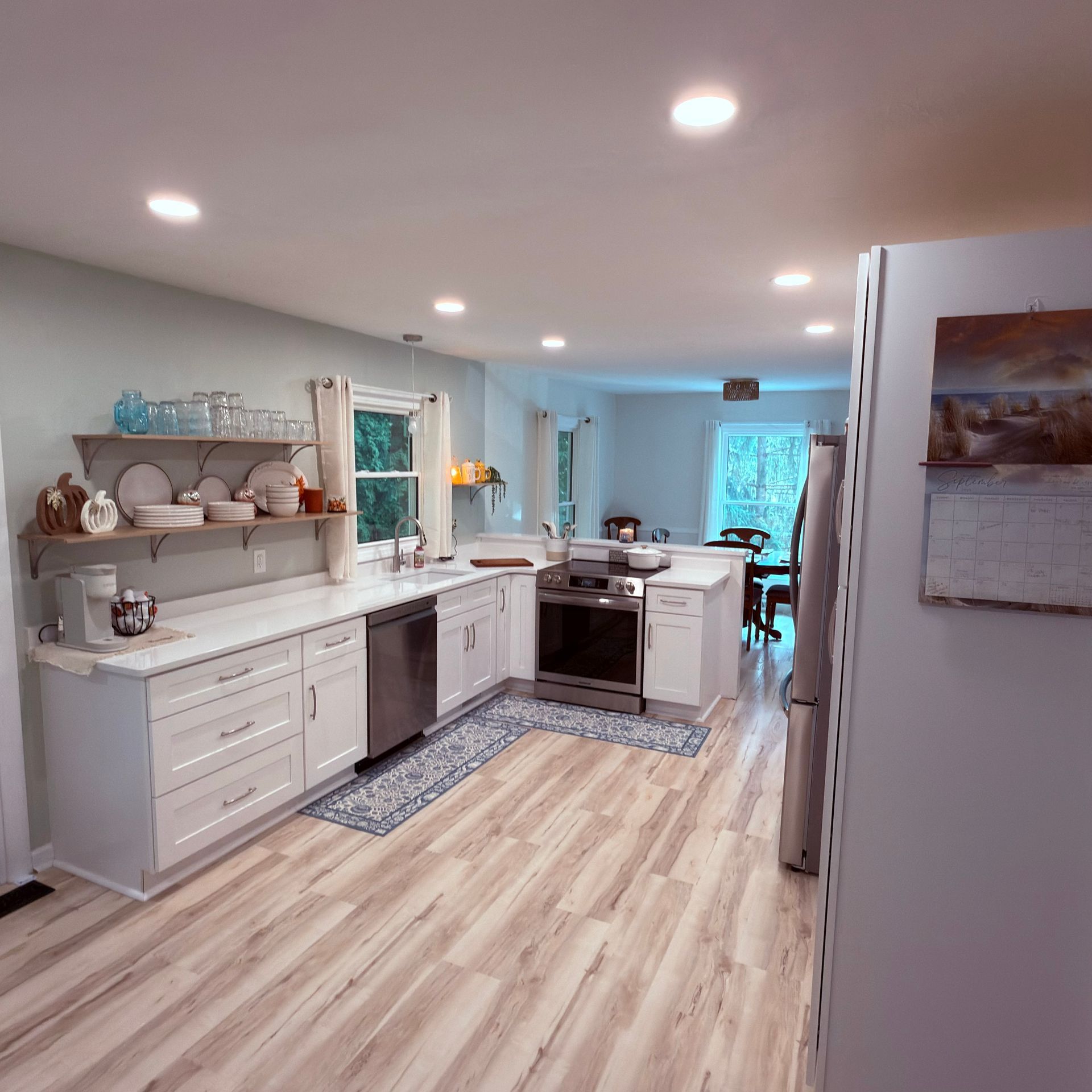 Bright modern kitchen with white cabinets, wood floors, stainless appliances, and a runner rug