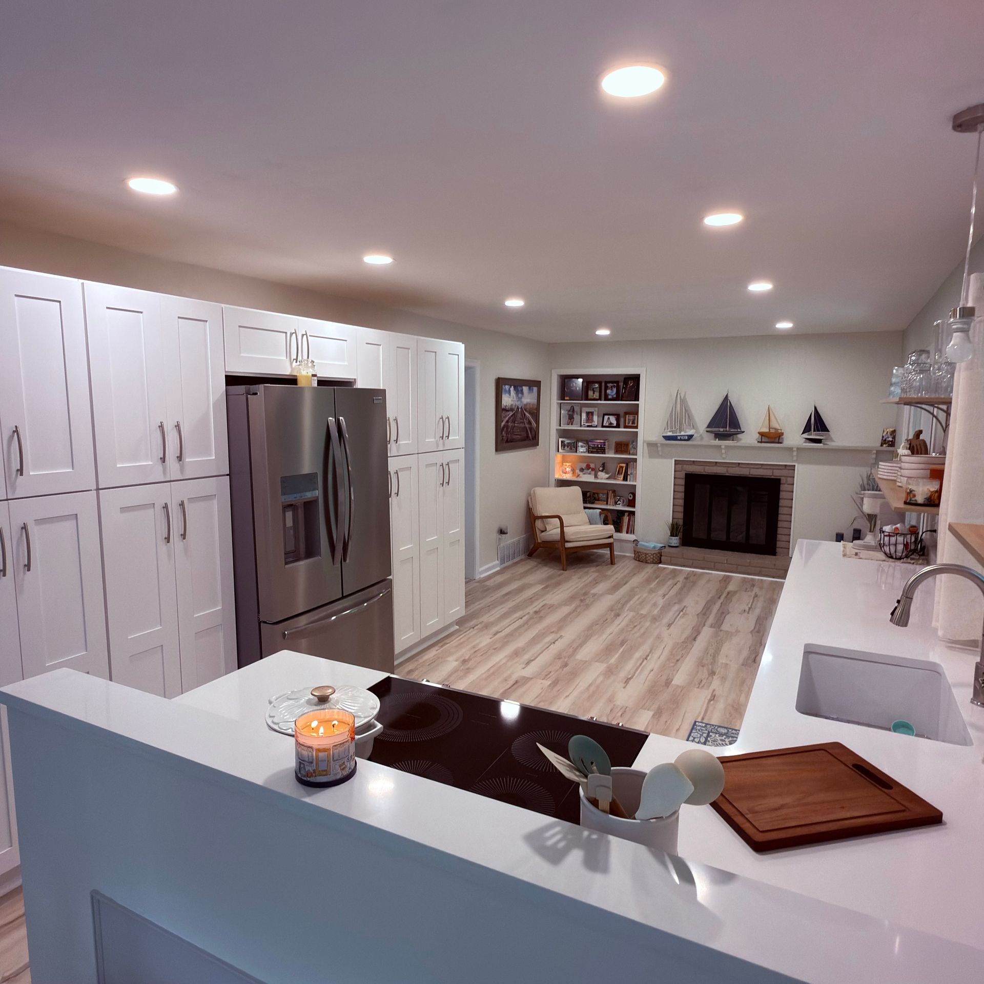 Modern white kitchen opening to a living room with fireplace, recessed lights, and wood flooring
