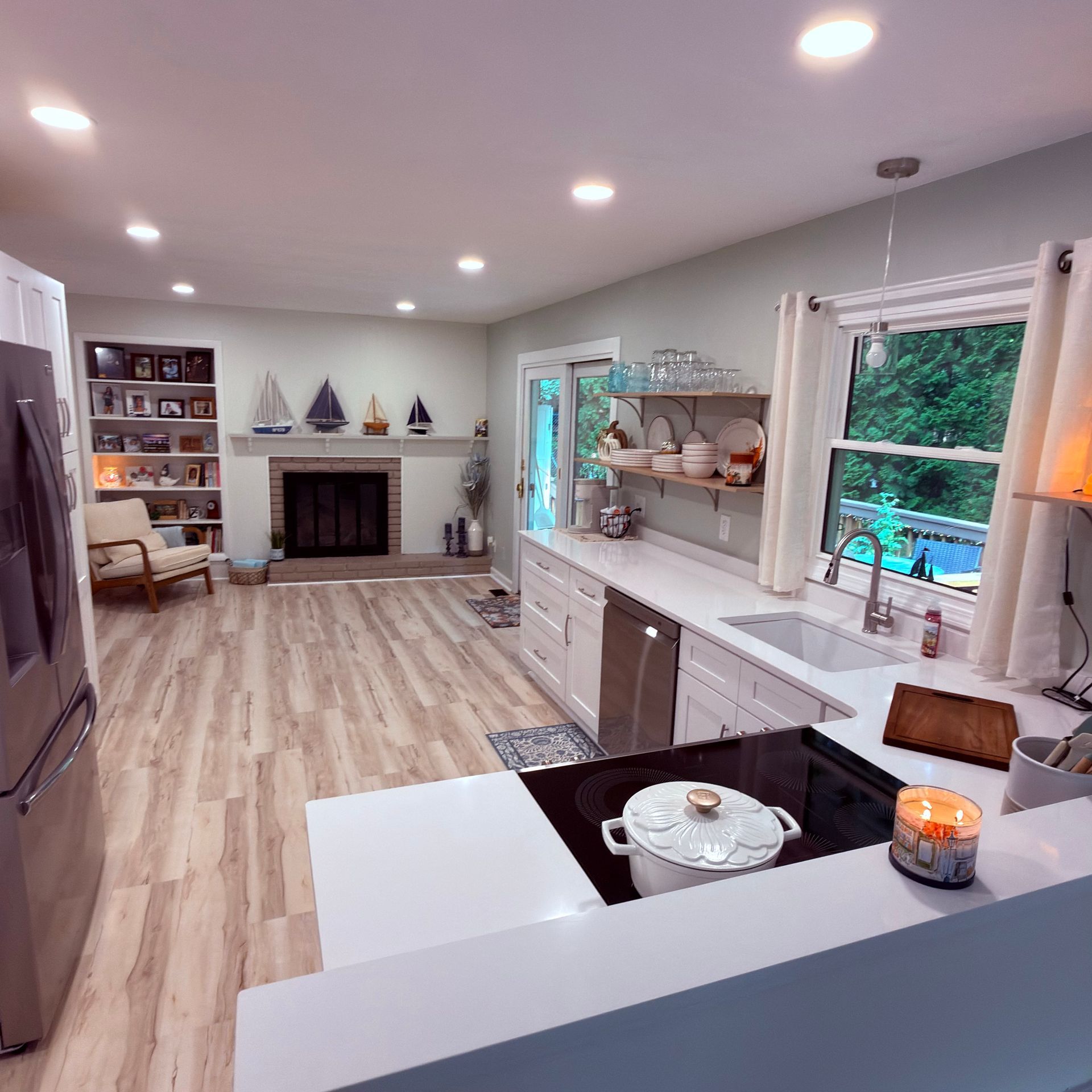 Bright open kitchen and living room with white cabinetry, island, fireplace, and large windows