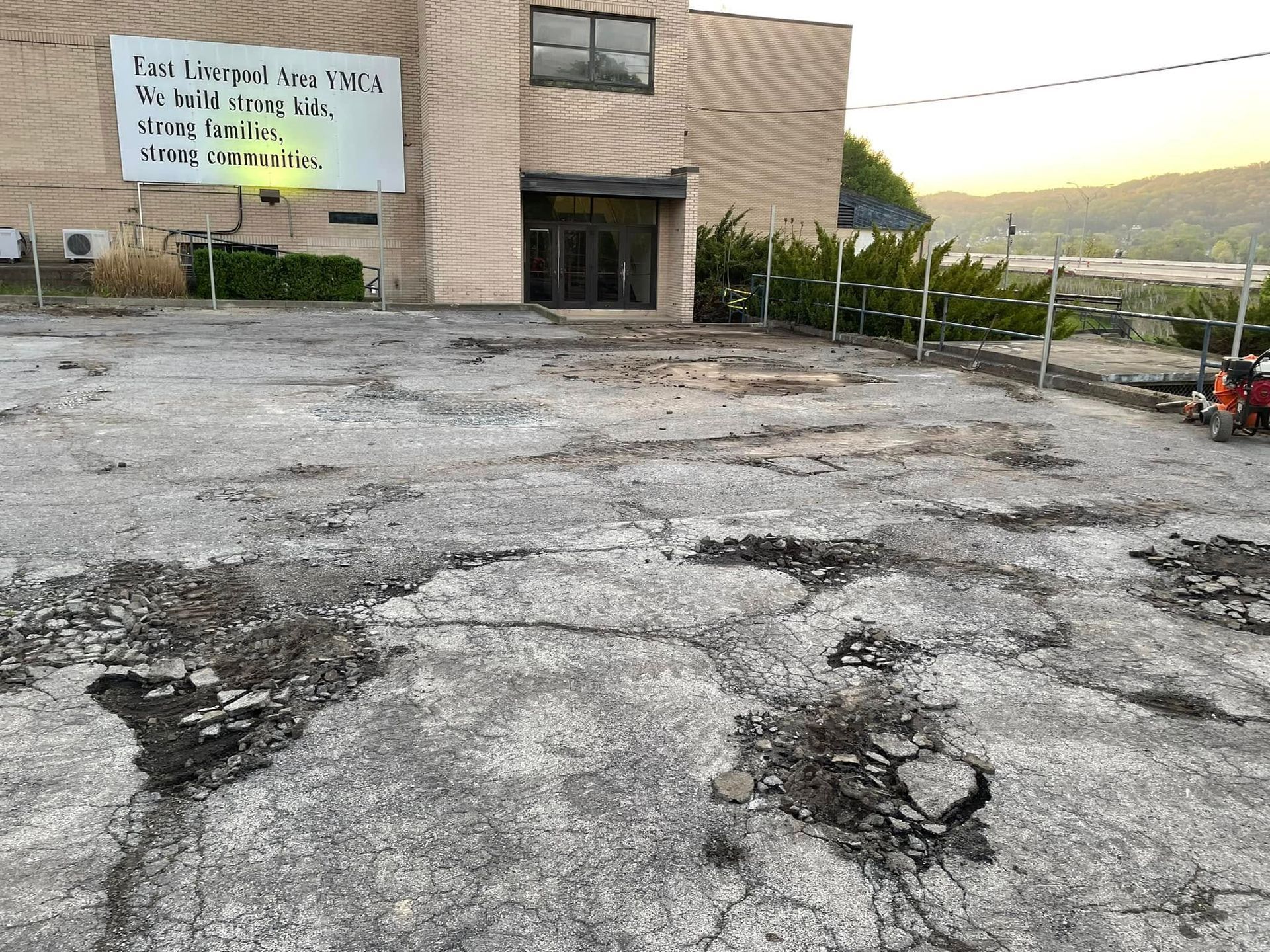 A crumbling, potholed parking lot in front of a tan building with a sign about East Liverpool.