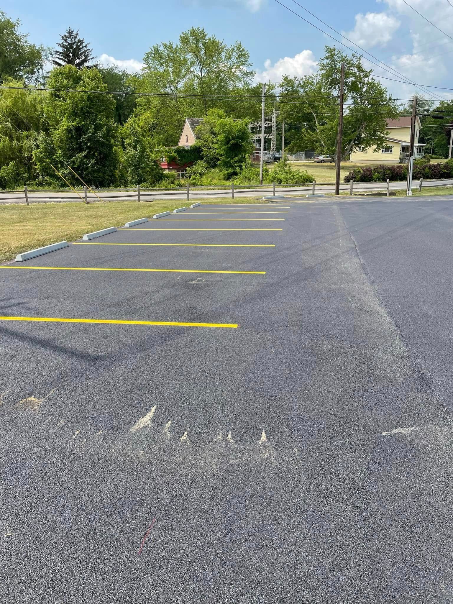 A paved parking lot with yellow-painted parking space lines and white parking curbs, set against a backdrop of trees.