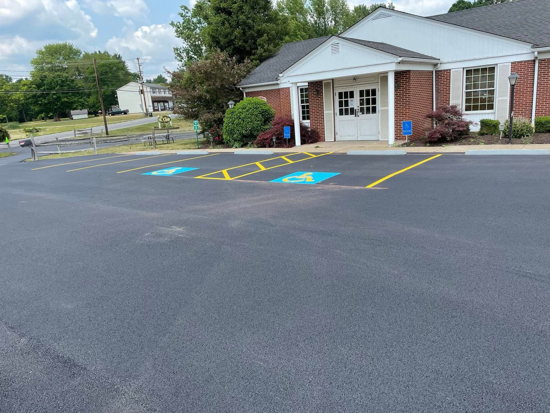 Two marked handicap parking spots in a paved parking lot in front of a white building with a brick exterior.