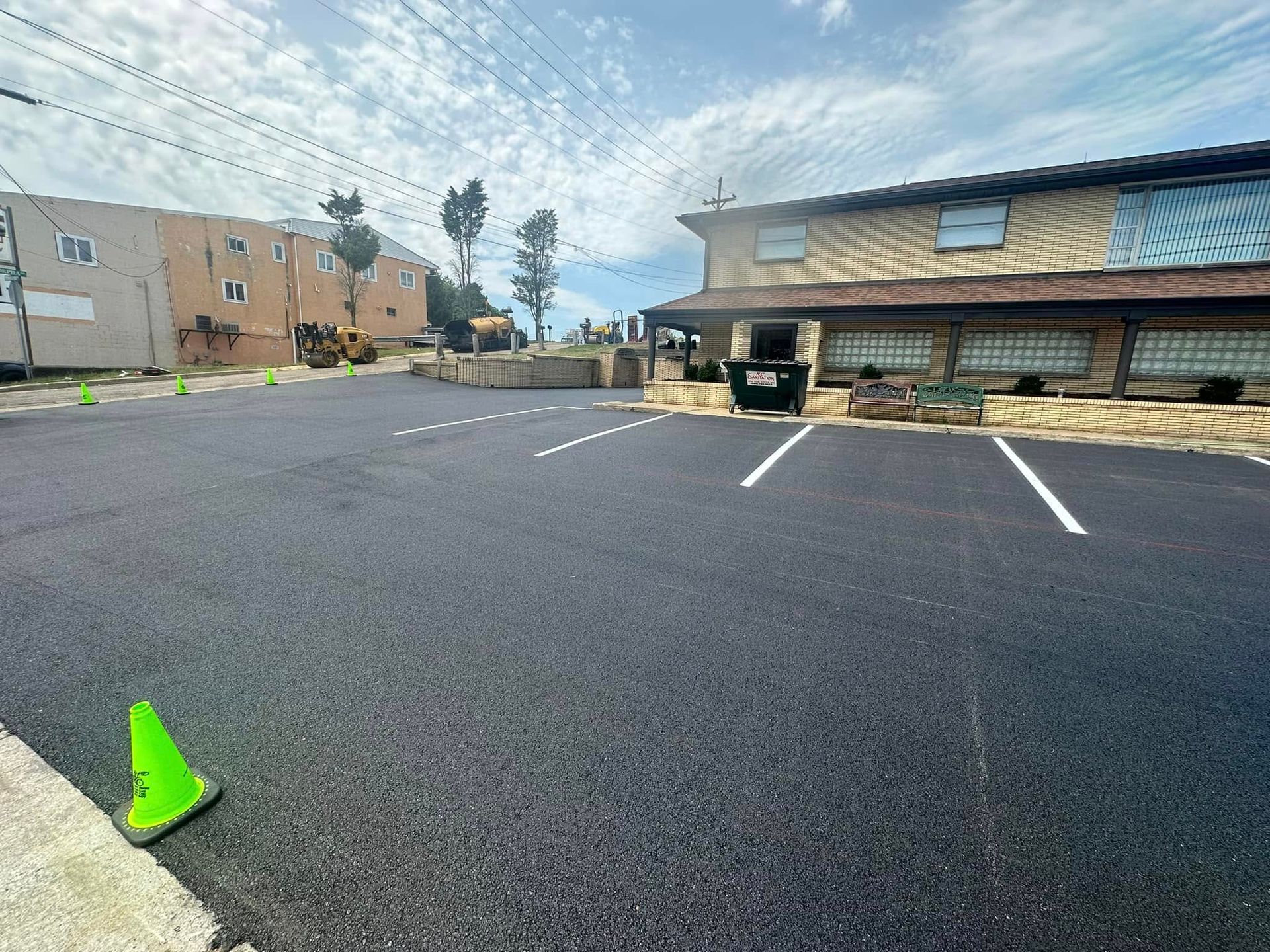 A newly paved asphalt parking lot with white-painted lines and bright green safety cones on a sunny day.