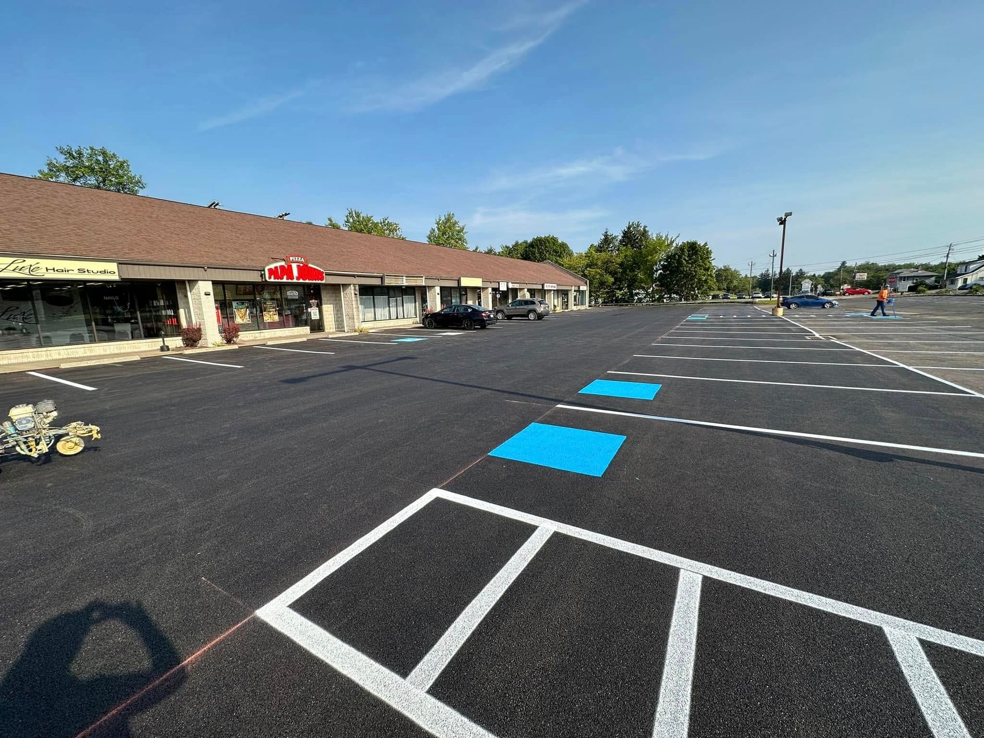 A newly paved parking lot featuring white-painted stall lines and blue-painted accessible parking spaces in front of shops.