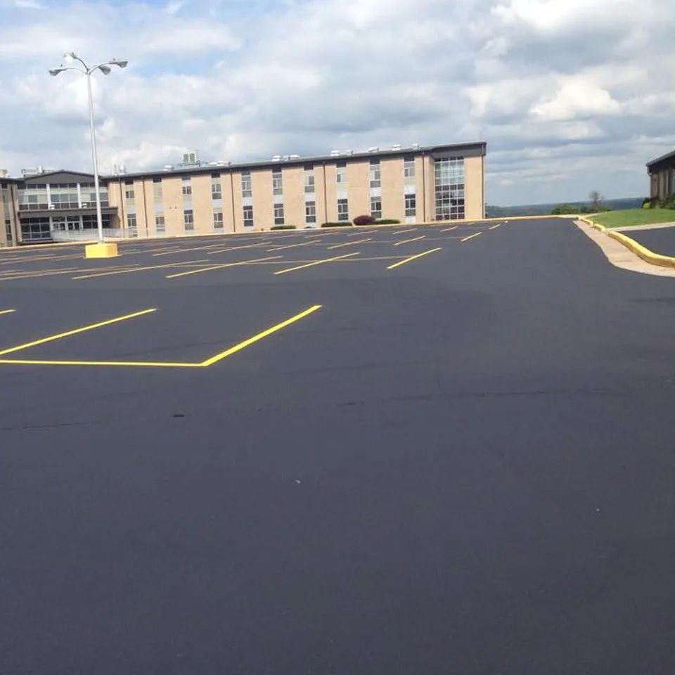 A large, freshly paved asphalt parking lot with yellow painted lines in front of a multi-story, light-colored building.