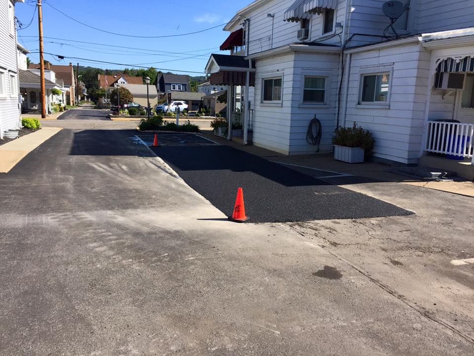 Freshly laid black asphalt patch on a driveway next to a white building under a bright blue sky.