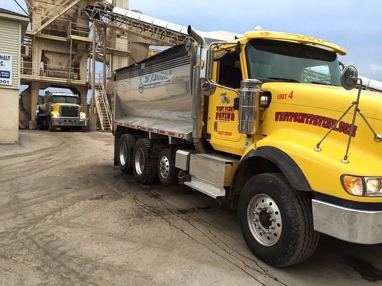 A bright yellow dump truck parked at a gravel site near a large industrial loading structure.