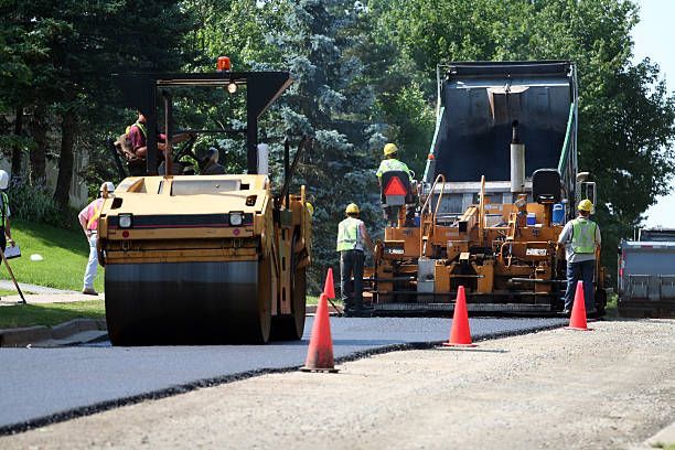 Road construction workers use a yellow asphalt roller and a paver to pave a new surface on a street.