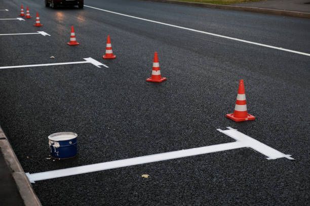 Orange traffic cones line a freshly painted white parking space on an asphalt road with a paint bucket nearby.