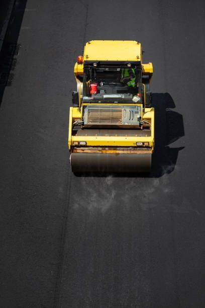 An overhead view of a yellow industrial steamroller compacting fresh, dark asphalt on a road.