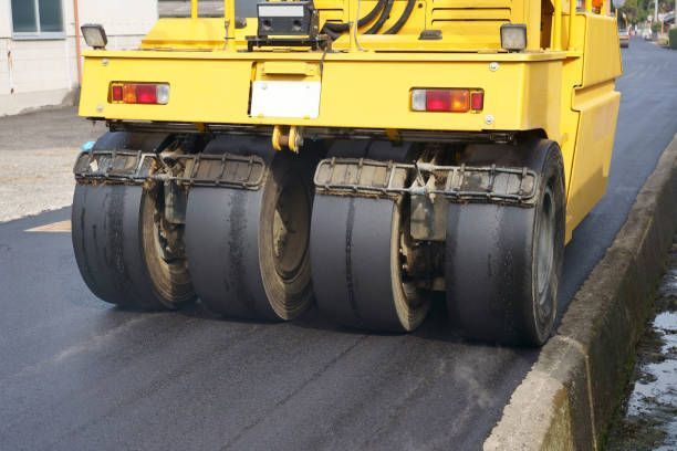 A yellow pneumatic-tired roller compacting a fresh asphalt road.