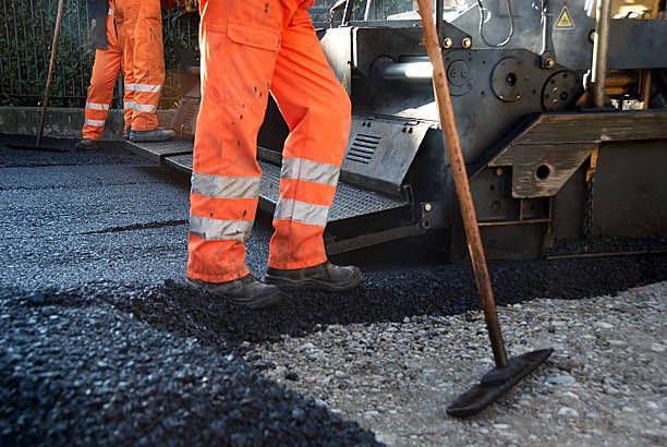 Construction workers in orange high-visibility gear paving a road with asphalt alongside machinery.