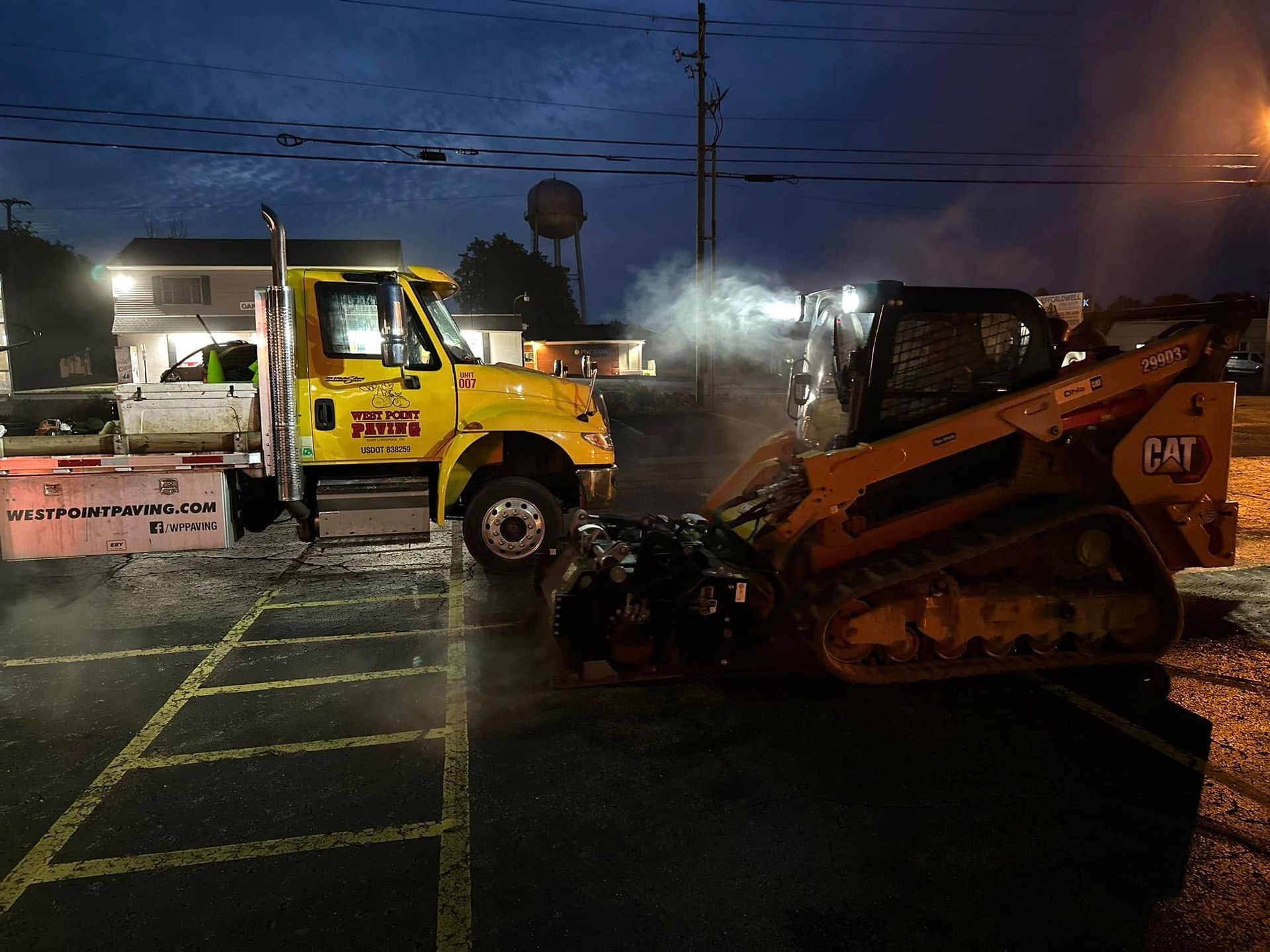 A yellow dump truck parked at dusk next to a Caterpillar track loader with steam rising from its engine.