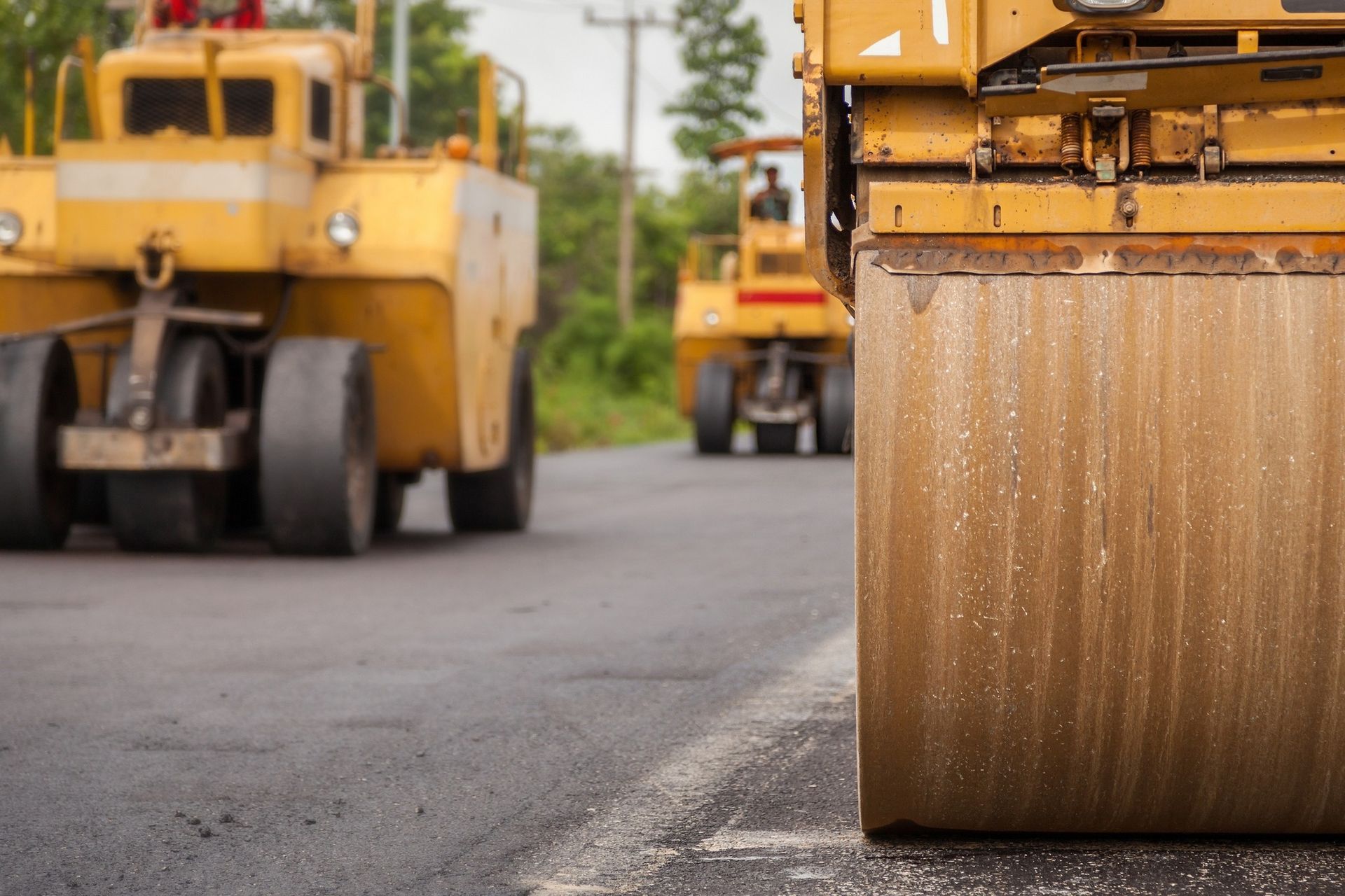 Yellow road construction rollers working on an asphalt road surface.