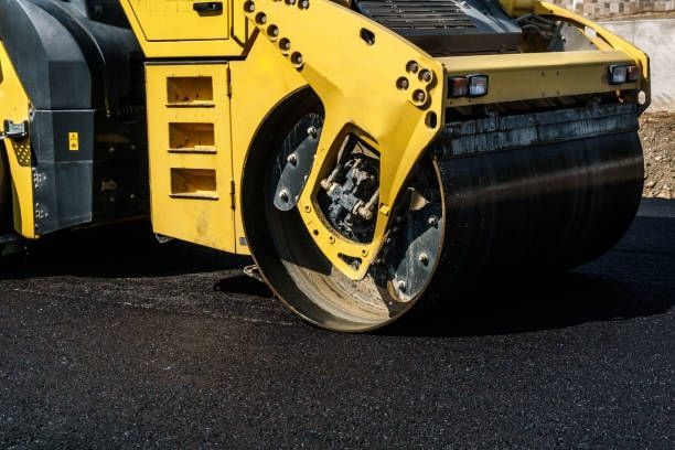 A yellow steamroller compacts fresh, dark asphalt on a construction site.