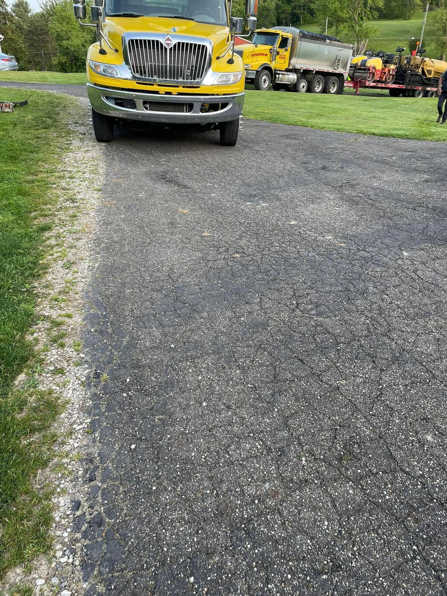 A yellow International truck sits on an asphalt driveway near a green, grassy area.