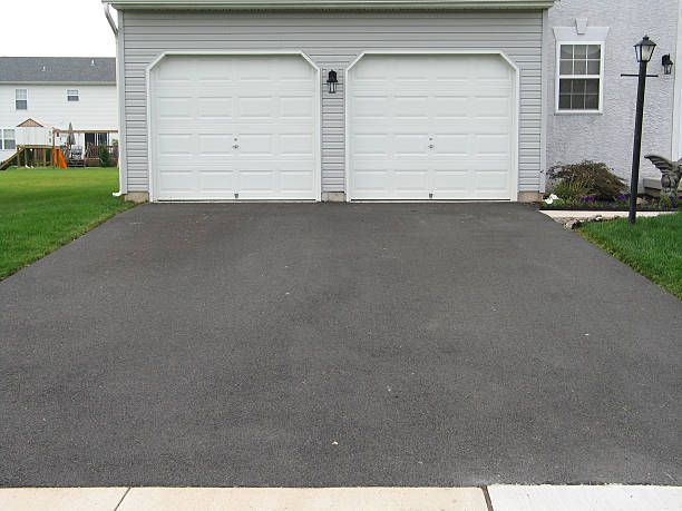 A two-car garage with white doors, gray siding, and an asphalt driveway in a suburban setting.