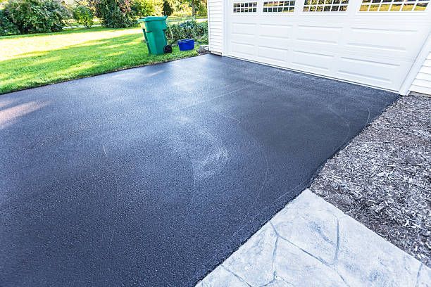 A freshly paved black asphalt driveway meeting a light-colored stamped concrete walkway in front of a white garage.