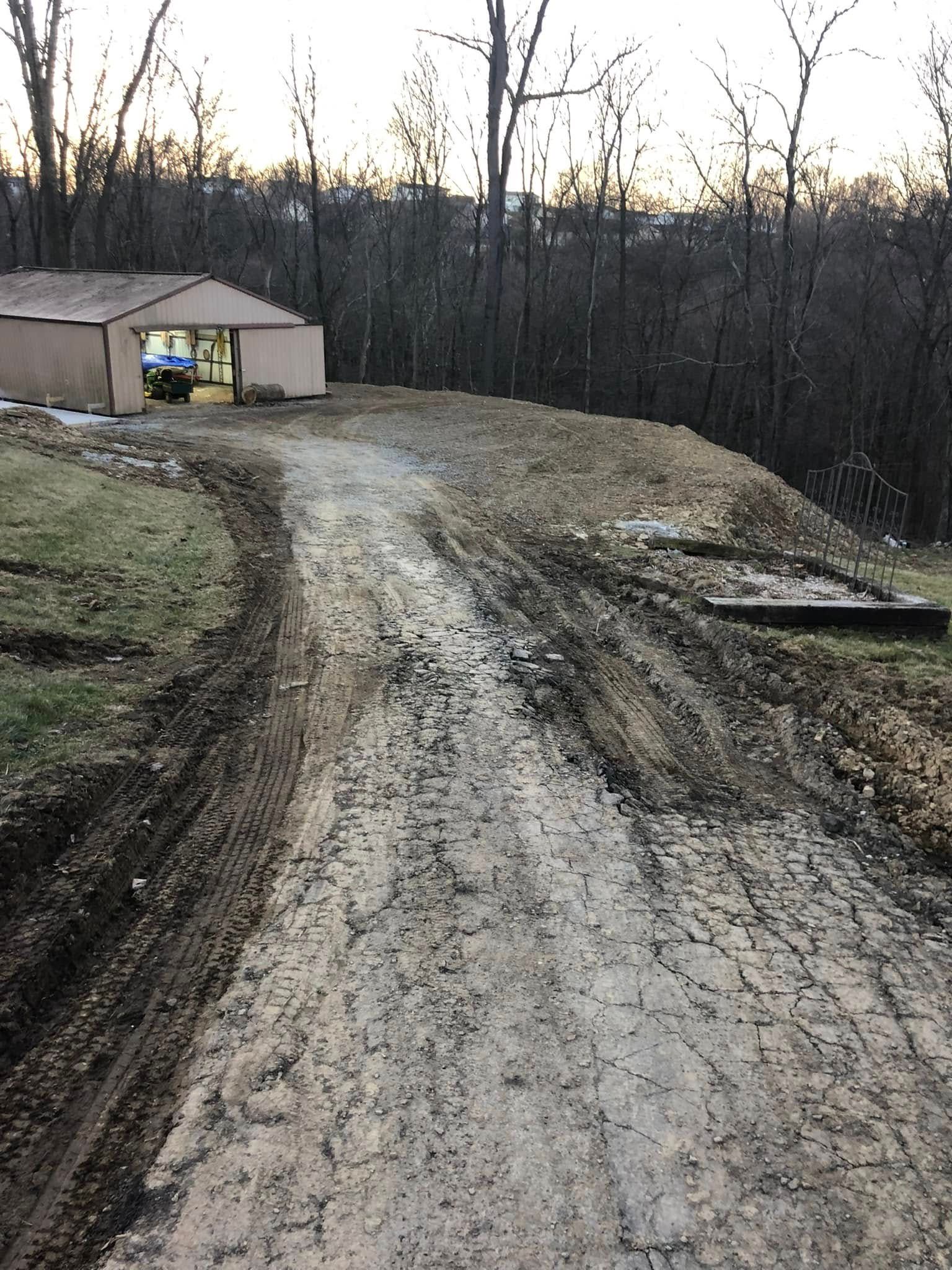 A gravel driveway leads toward a tan building near a line of bare trees on a cloudy day.