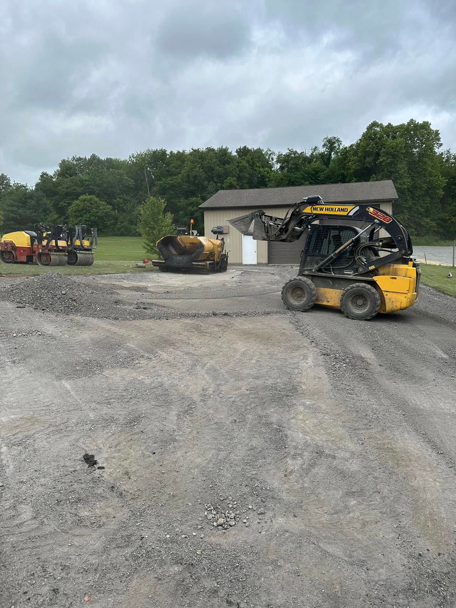 Yellow skid steer loader and a small construction vehicle on a gravel lot in front of a storage shed.