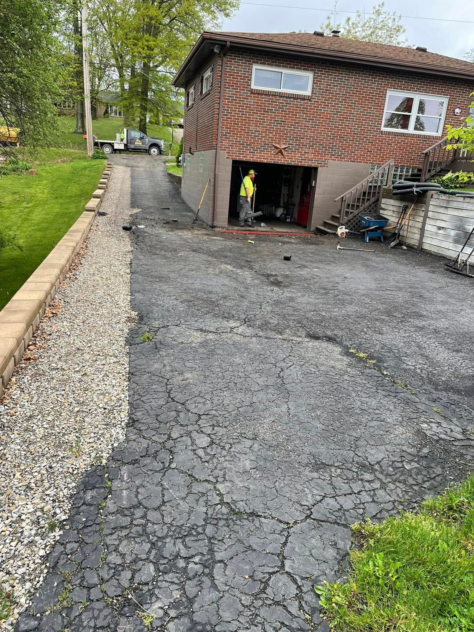 A house with a patterned brown facade and a gravel driveway, featuring a person standing in the open garage entrance.