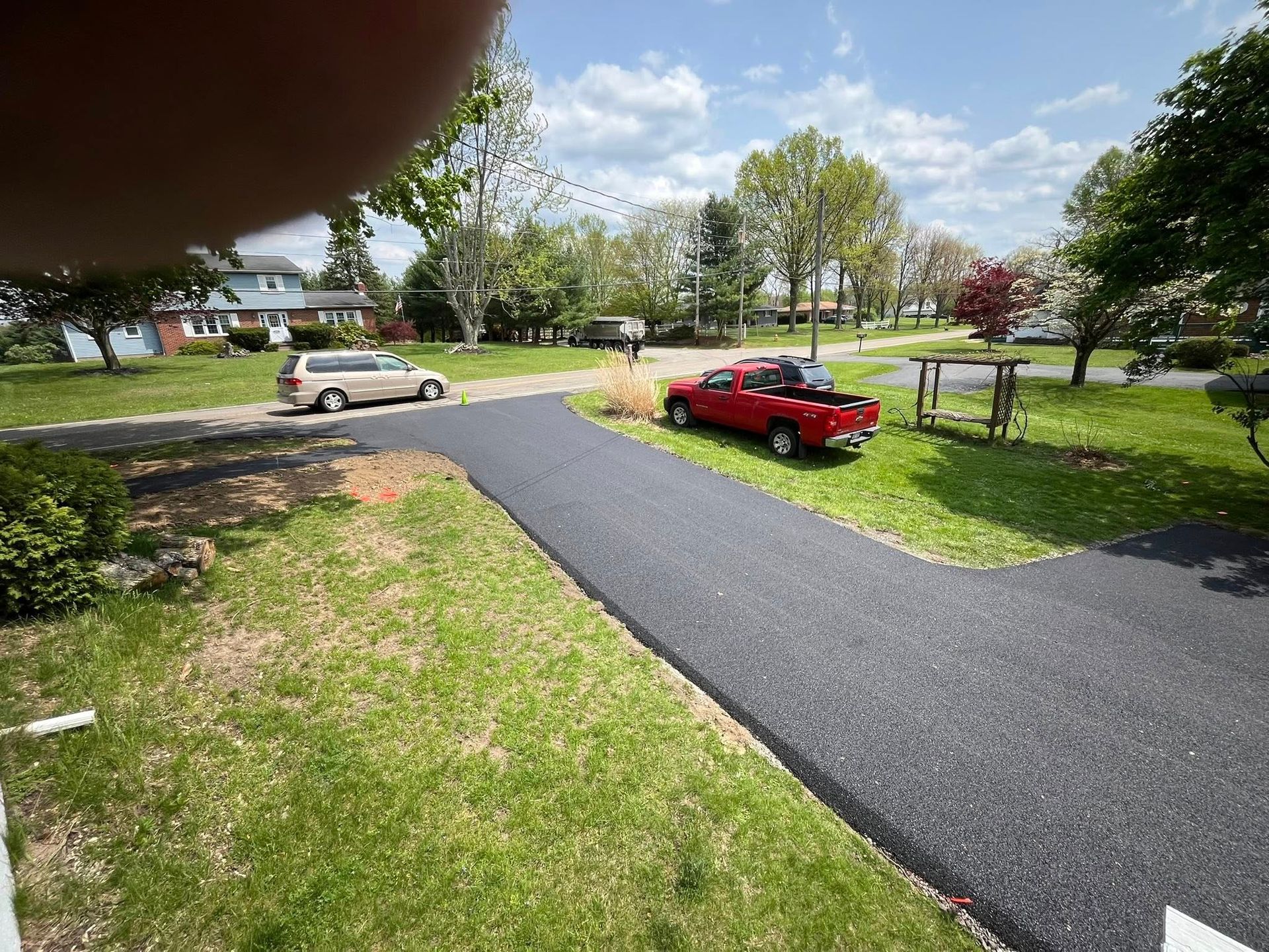 A newly paved asphalt driveway leads to a suburban home with a red truck parked on the side.