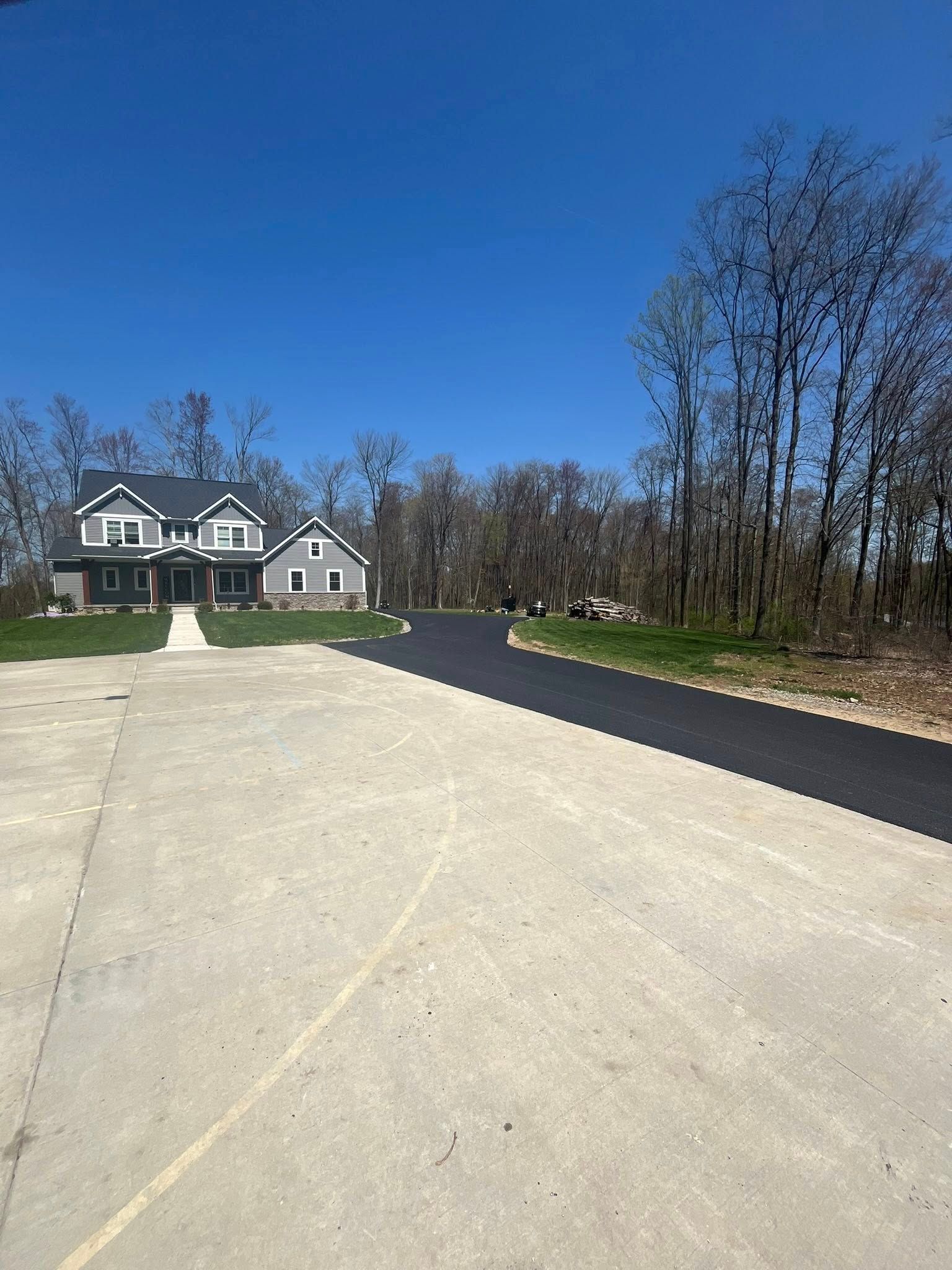 A house with a light-colored concrete driveway transitioning into a newly paved black asphalt driveway.