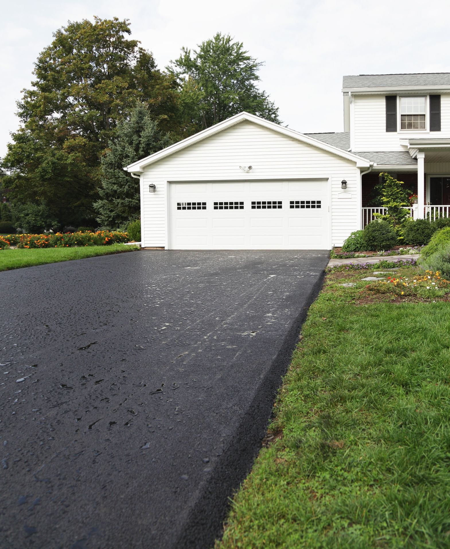 A fresh, black asphalt driveway leading to a white, two-car garage attached to a white suburban home.