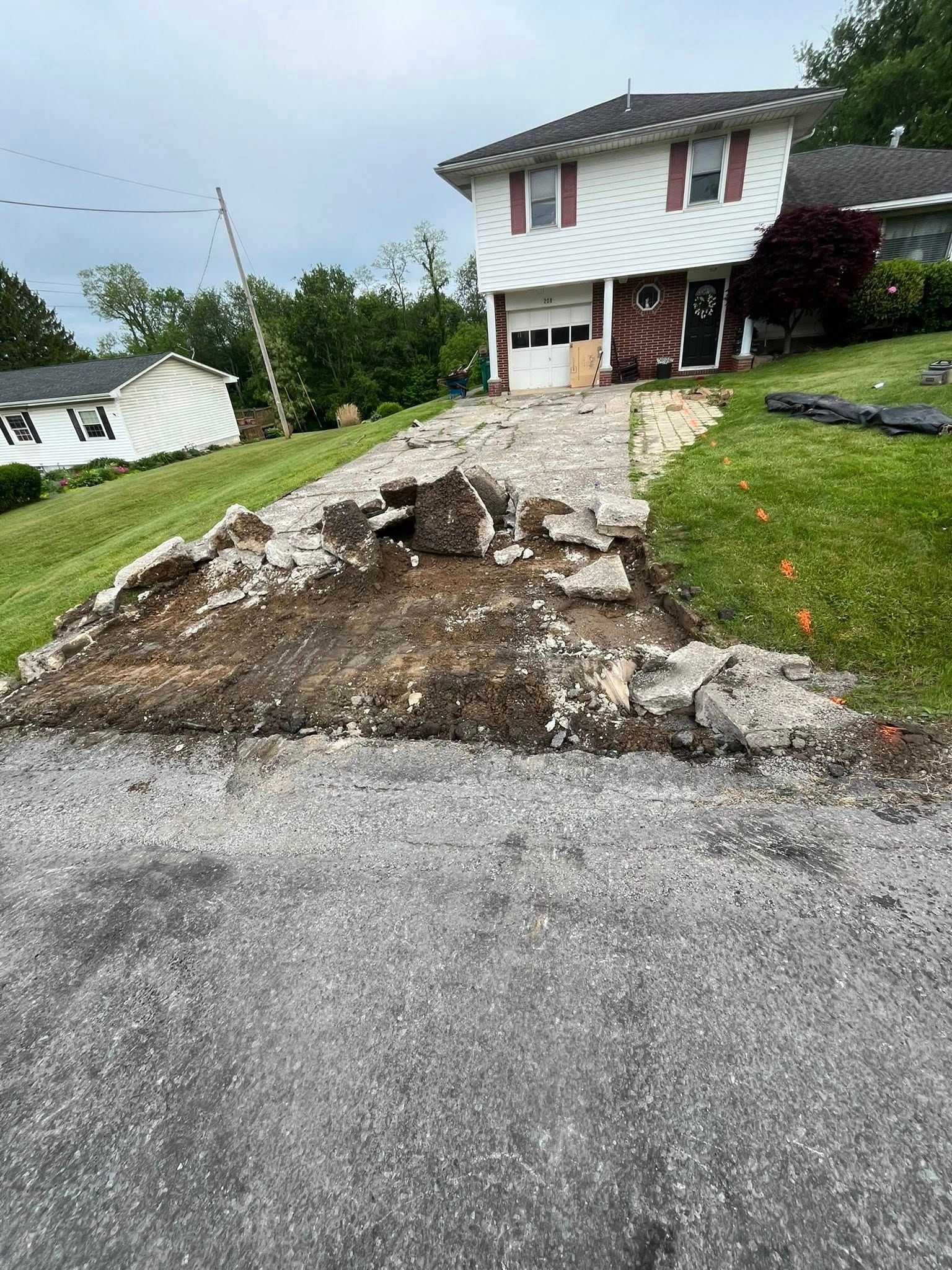A white two-story house with a damaged, partially removed concrete driveway leading to the garage.