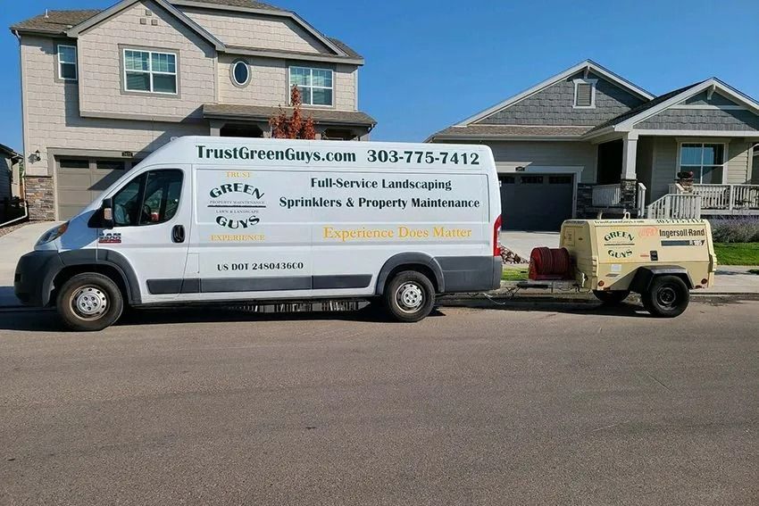 White van with landscaping company logo parked in front of houses with a trailer.