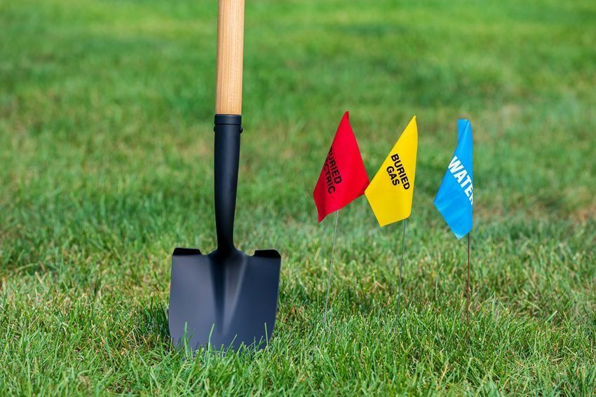 A shovel next to three colored flags in a grassy lawn. The flags mark utilities like water.