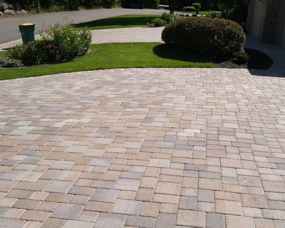 Brick paver driveway leading to green lawn and shrubs.
