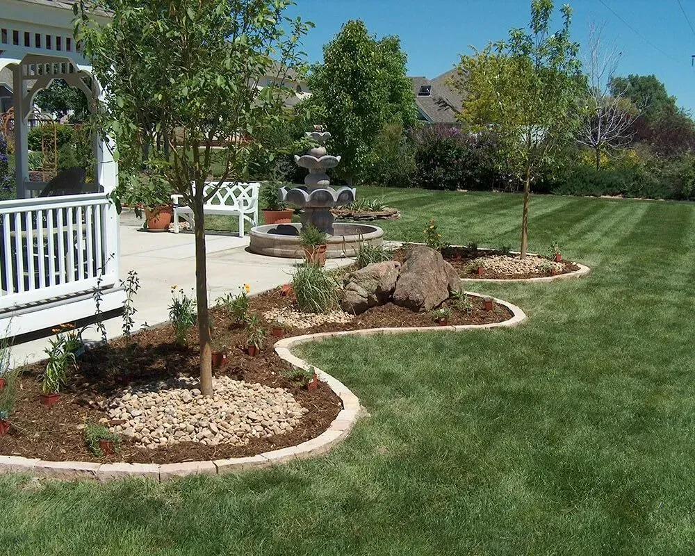 Lush green lawn with garden beds, a fountain, and a gazebo on a sunny day.