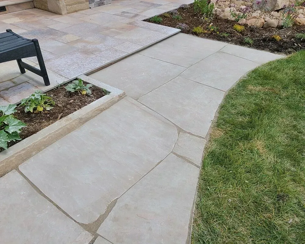 Stone pathway curves through a grassy area, alongside a garden bed and patio.