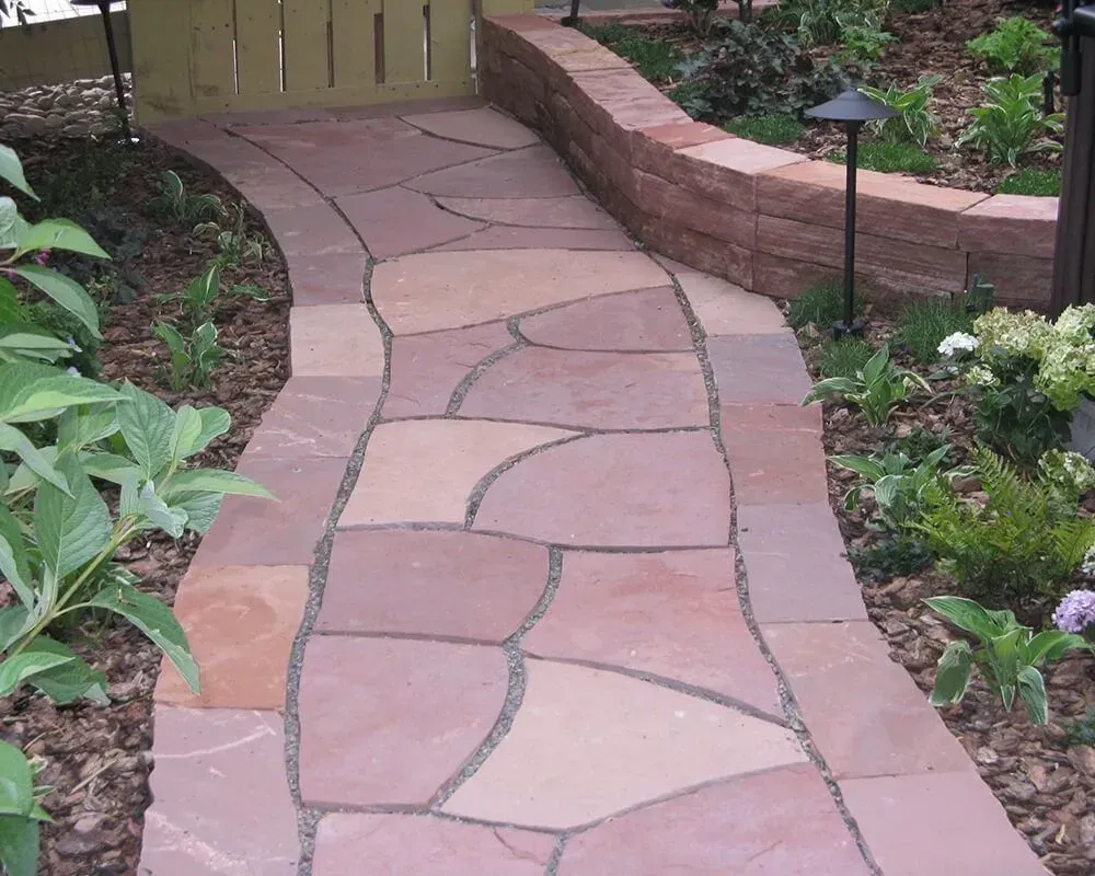 Flagstone pathway winds through a garden with a retaining wall and plants.