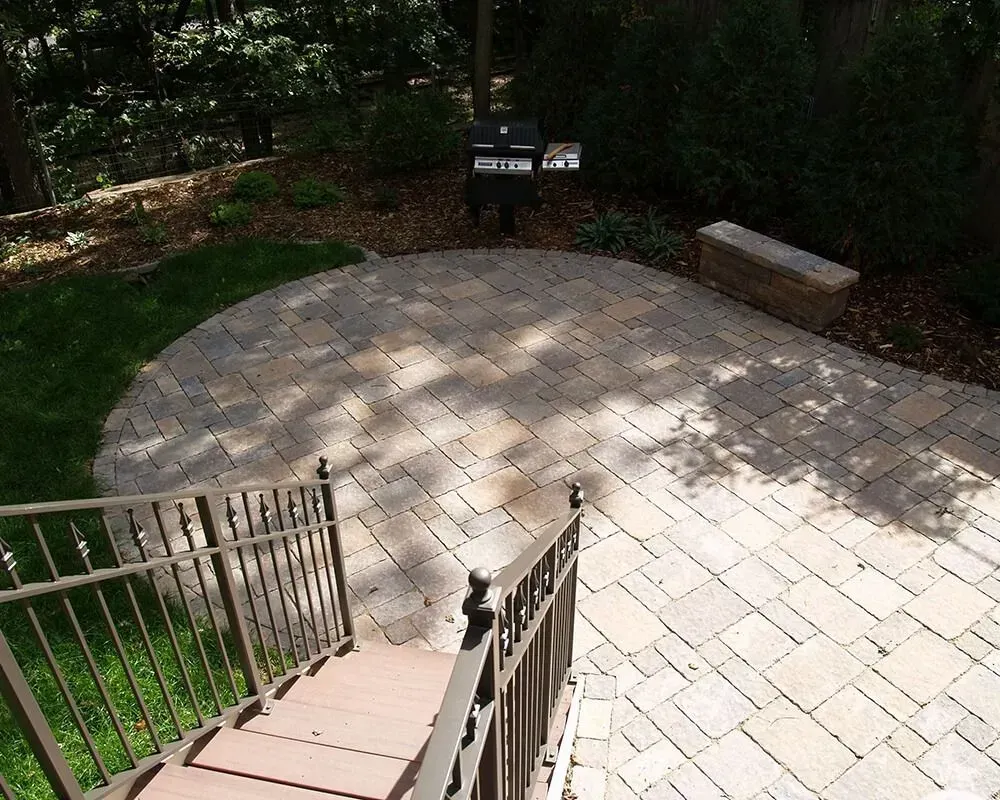 Stone patio with stairs, grill, and surrounding greenery.