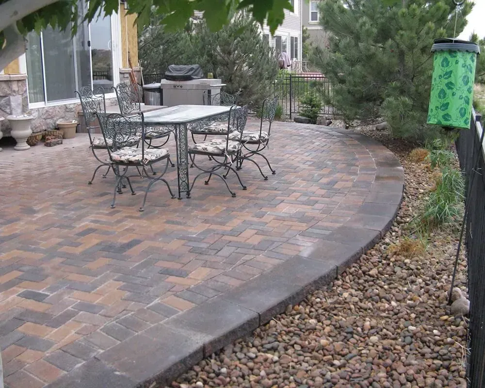 Brick patio with wrought iron table and chairs, bordered by stones and landscaping.