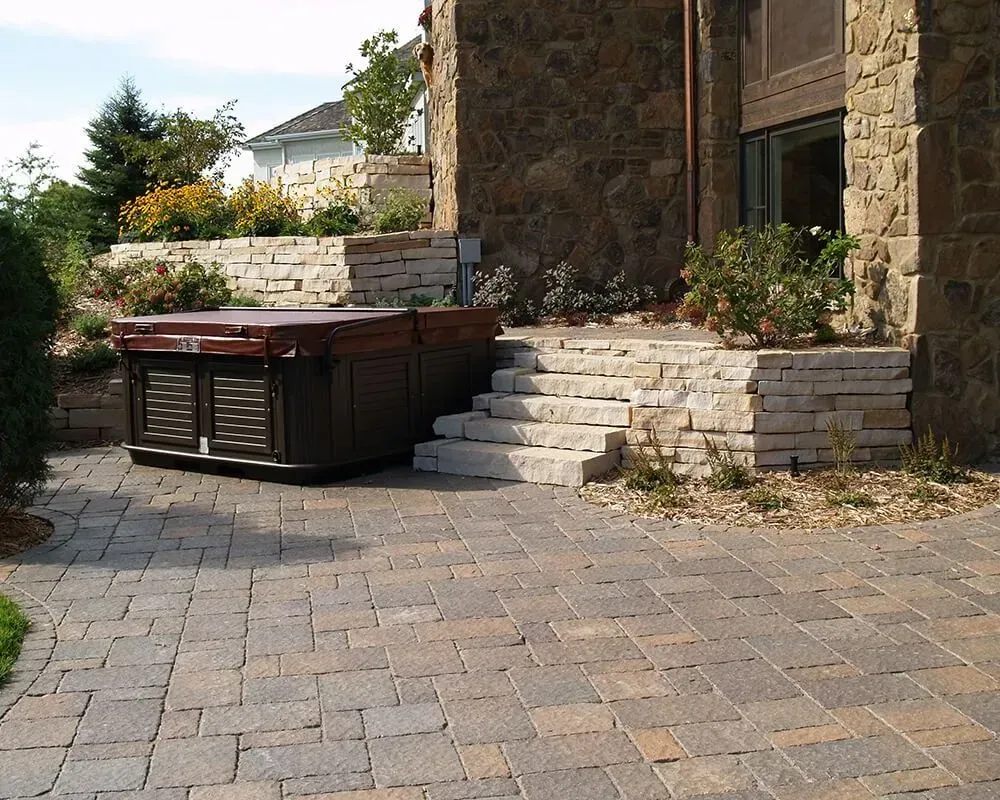 Hot tub on stone patio next to stone steps and building.